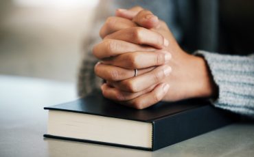 Bible book, person or hands praying for hope, help or support in Christianity religion or holy faith on table. Believe, prayer or woman studying or worshipping God in spiritual literature at home.